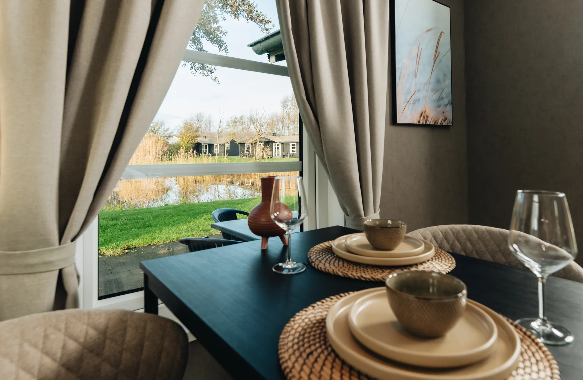 Uitzicht vanuit de lodge op een vijver en groene omgeving van Resort Land & Zee, met op de achtergrond andere houten vakantieverblijven aan het water.